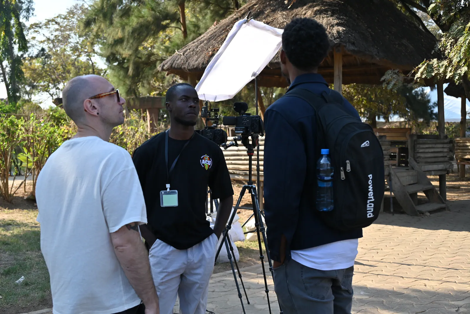 A crew sets up a camera and softbox beside a thatched shelter in Zambia.