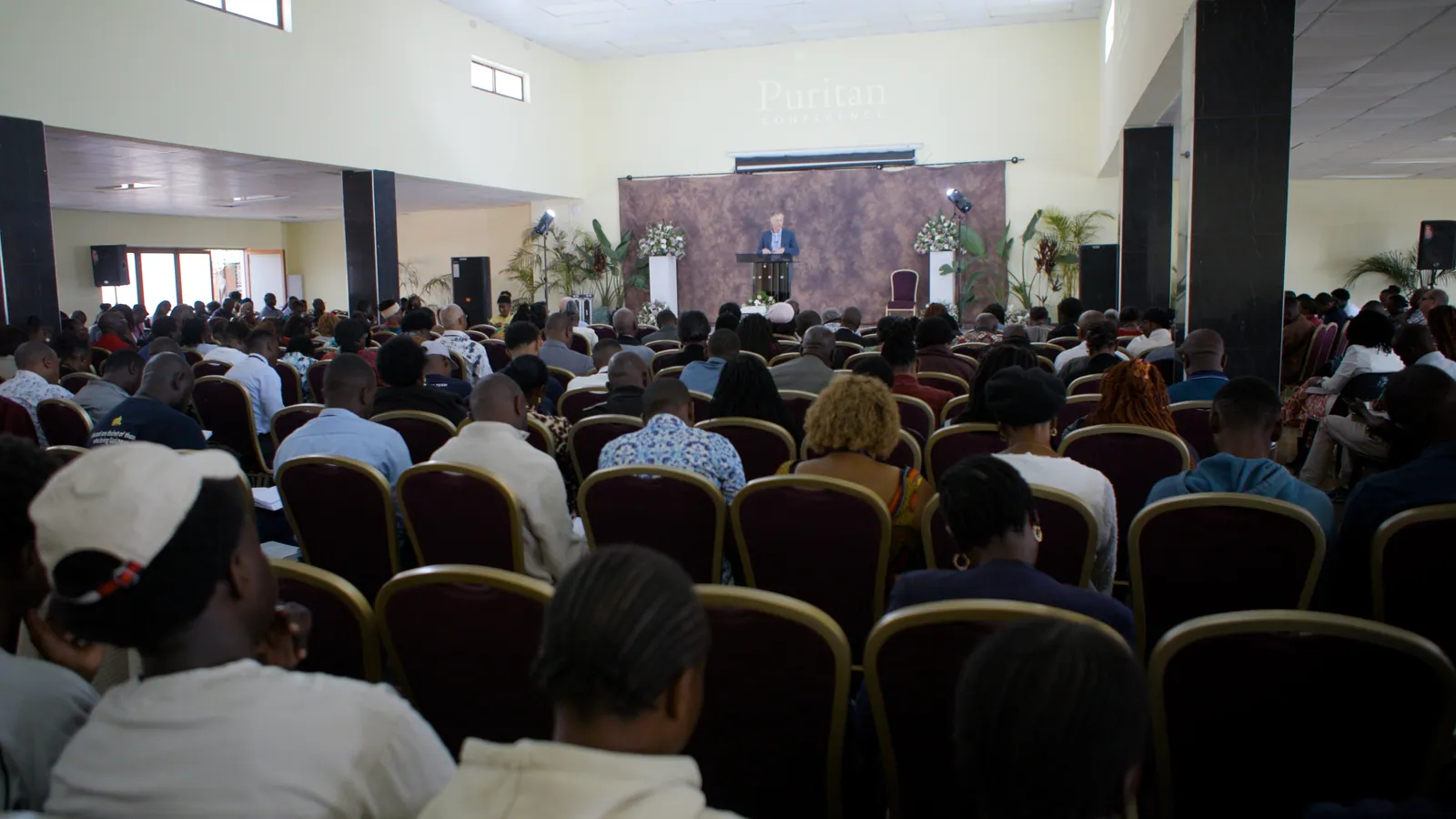 A packed conference hall in Lusaka, seen from the back, with a speaker at the far stage.