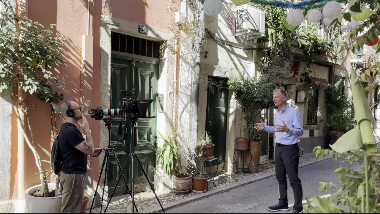 A film crew records Dr. Stephen Yuille in a narrow Lisbon street hung with lanterns.